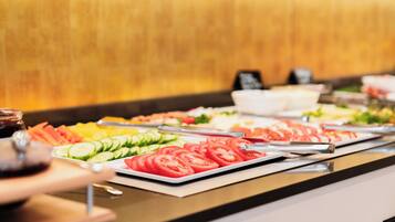 A buffet with various food items including sliced tomatoes, cucumbers, and other vegetables.