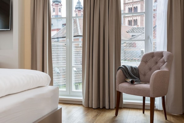 Habitación de hotel con cama, una silla y un ventanal con cortinas.