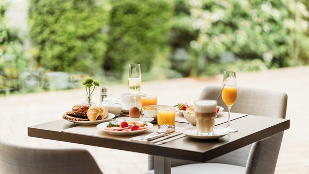 A breakfast table set outdoors with a variety of food and drinks, including croissants, eggs, and juice.