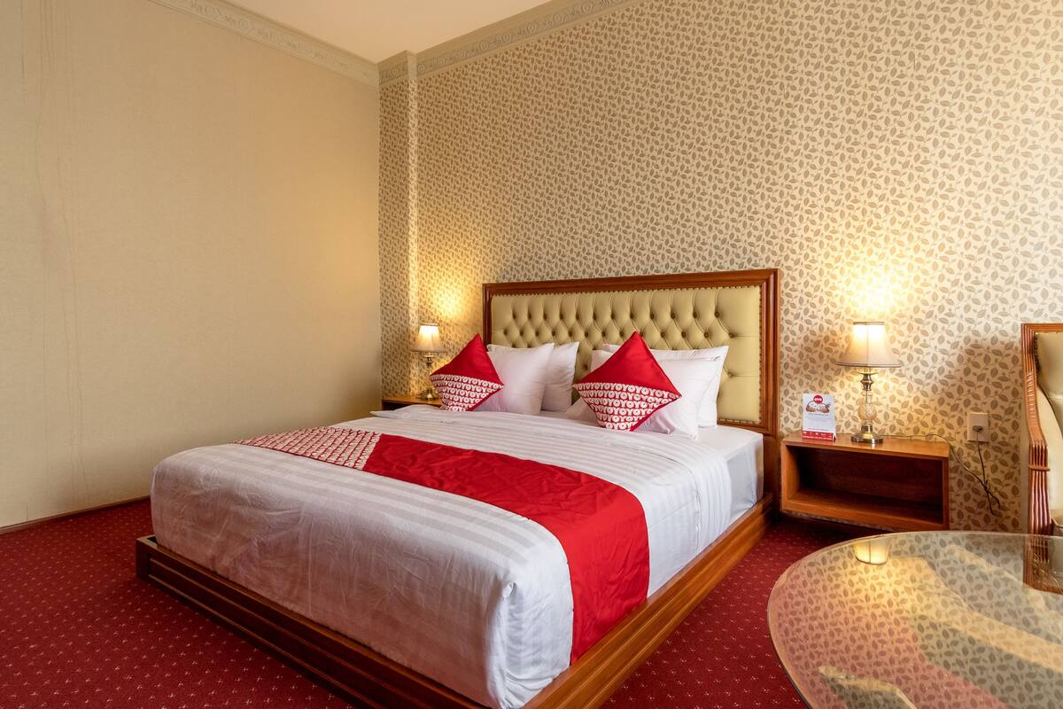 A hotel room with a large bed, two bedside tables, a round glass table, and patterned wallpaper.