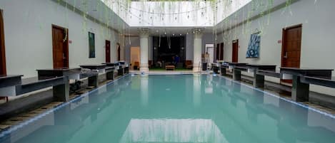 Una amplia piscina interior con una zona de estar central, rodeada de bancos y columnas.