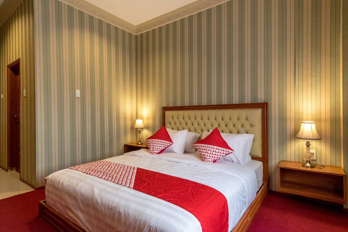 A hotel room with a large bed, striped wallpaper, and two bedside lamps.