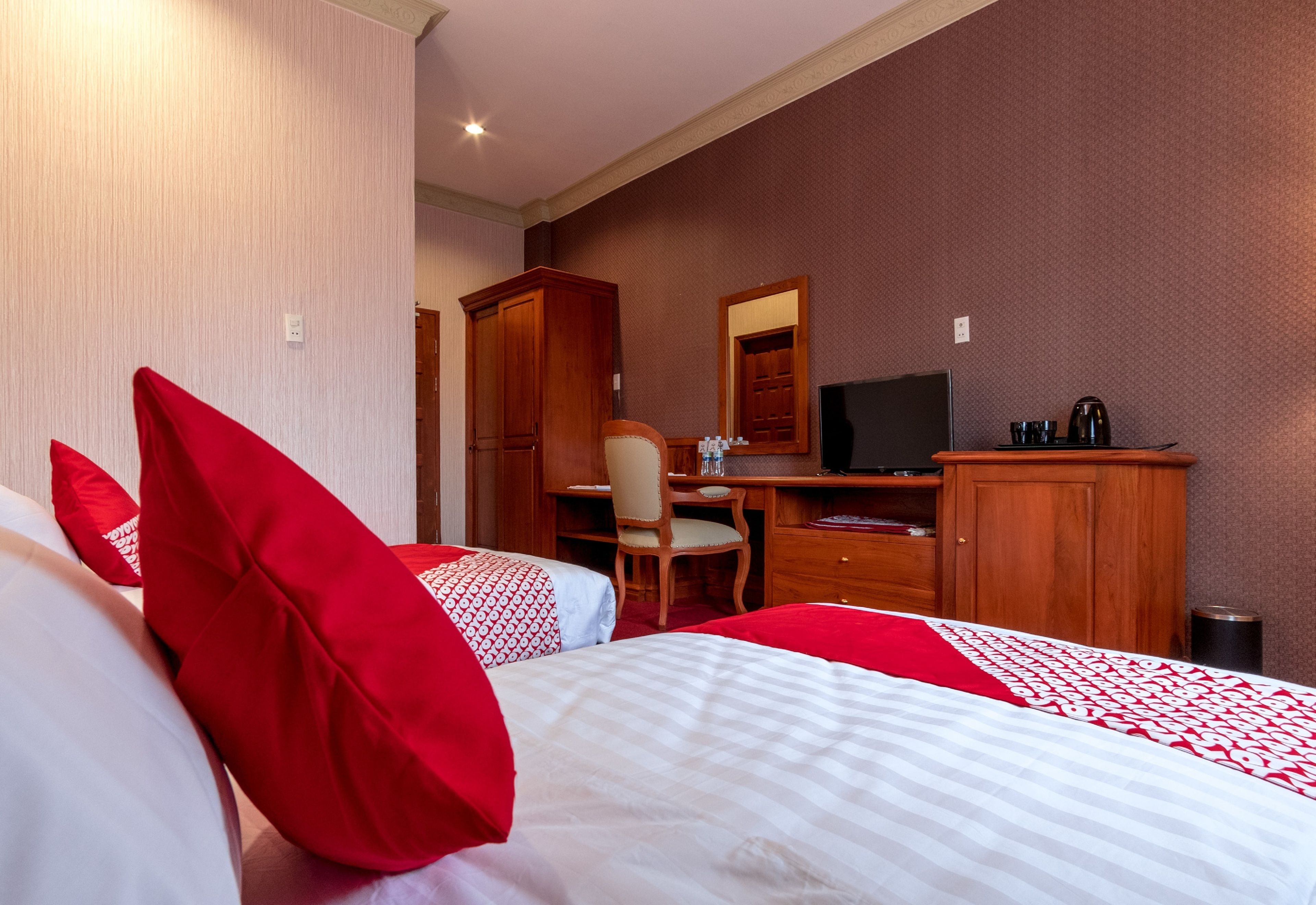 Quarto de hotel com duas camas, uma escrivaninha, uma cadeira, uma televisão e um guarda-roupa.