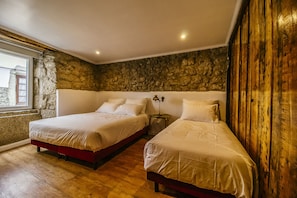 Quarto com duas camas, parede de pedra e piso de madeira.