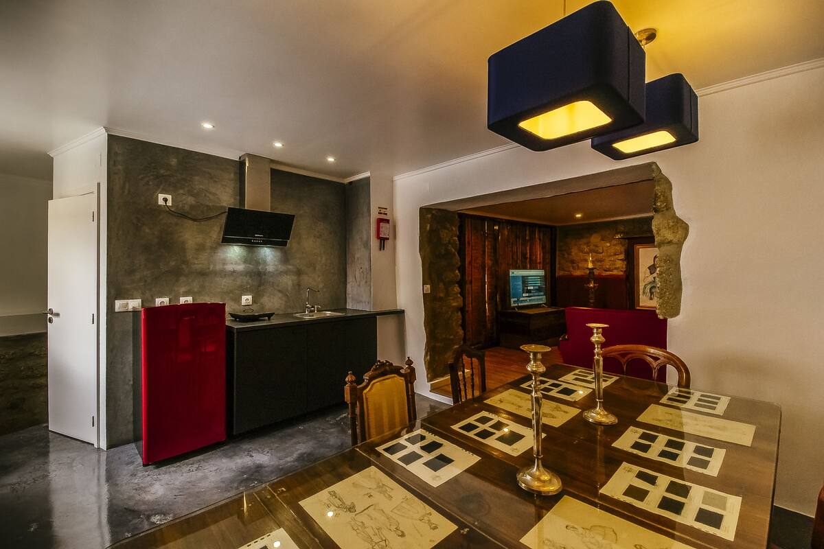 Une cuisine moderne avec un réfrigérateur rouge, un coin repas doté d’une table en bois et un mur en pierre.