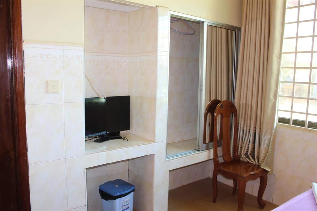 Ein Zimmer mit Fernseher auf einem Regal, einem Sessel, einem Fenster mit Vorhängen und einem Mülleimer.