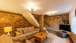 Una sala de estar acogedora con una pared de piedra, un sofá, una mesa de centro y un televisor.