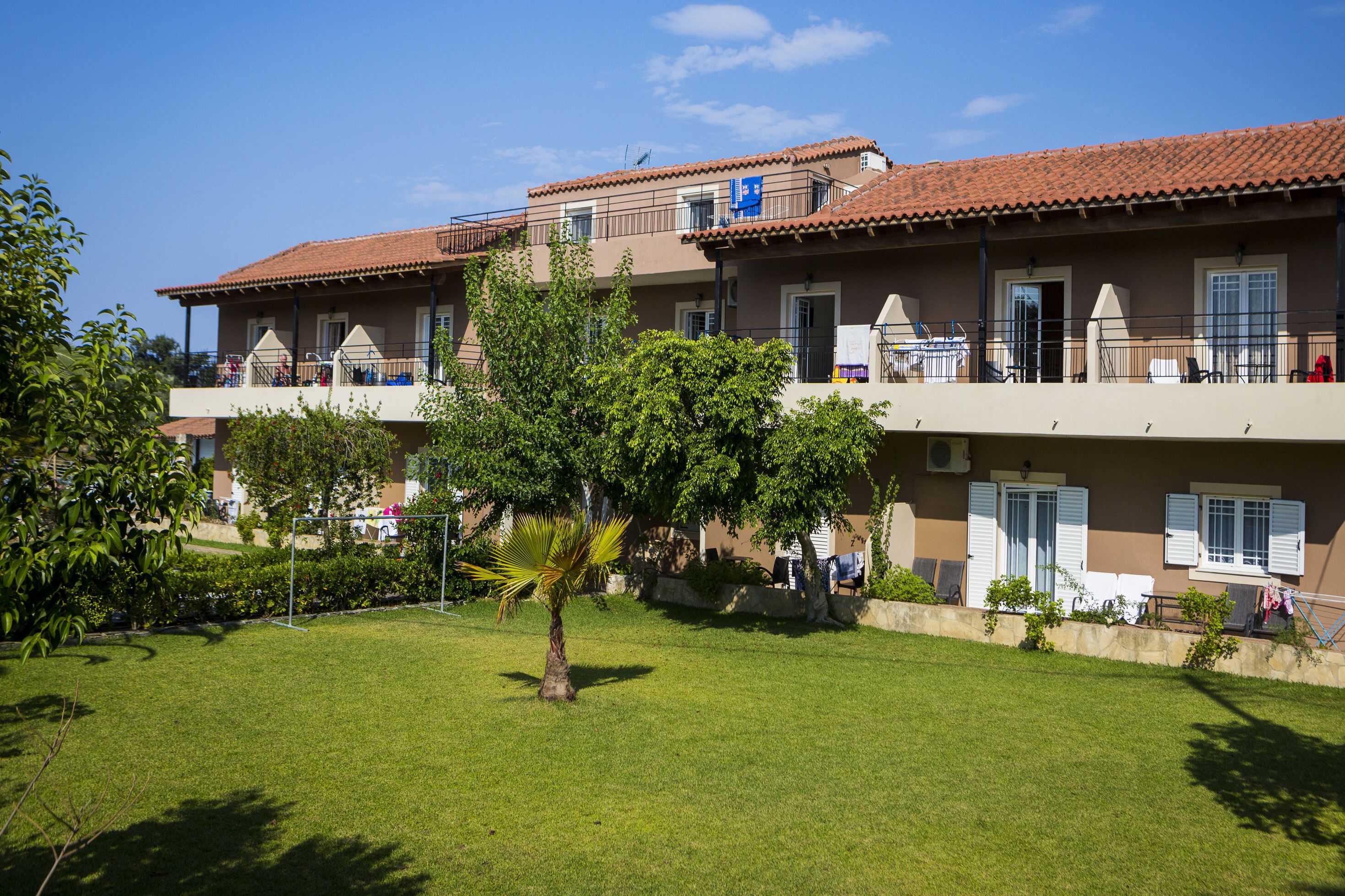 A two-story building with balconies, a lawn, and a palm tree.