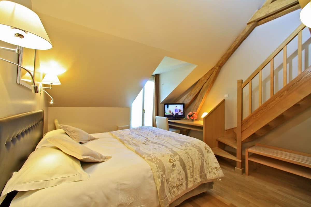 Een slaapkamer met een bed, een bureau met een computer en een houten trap.