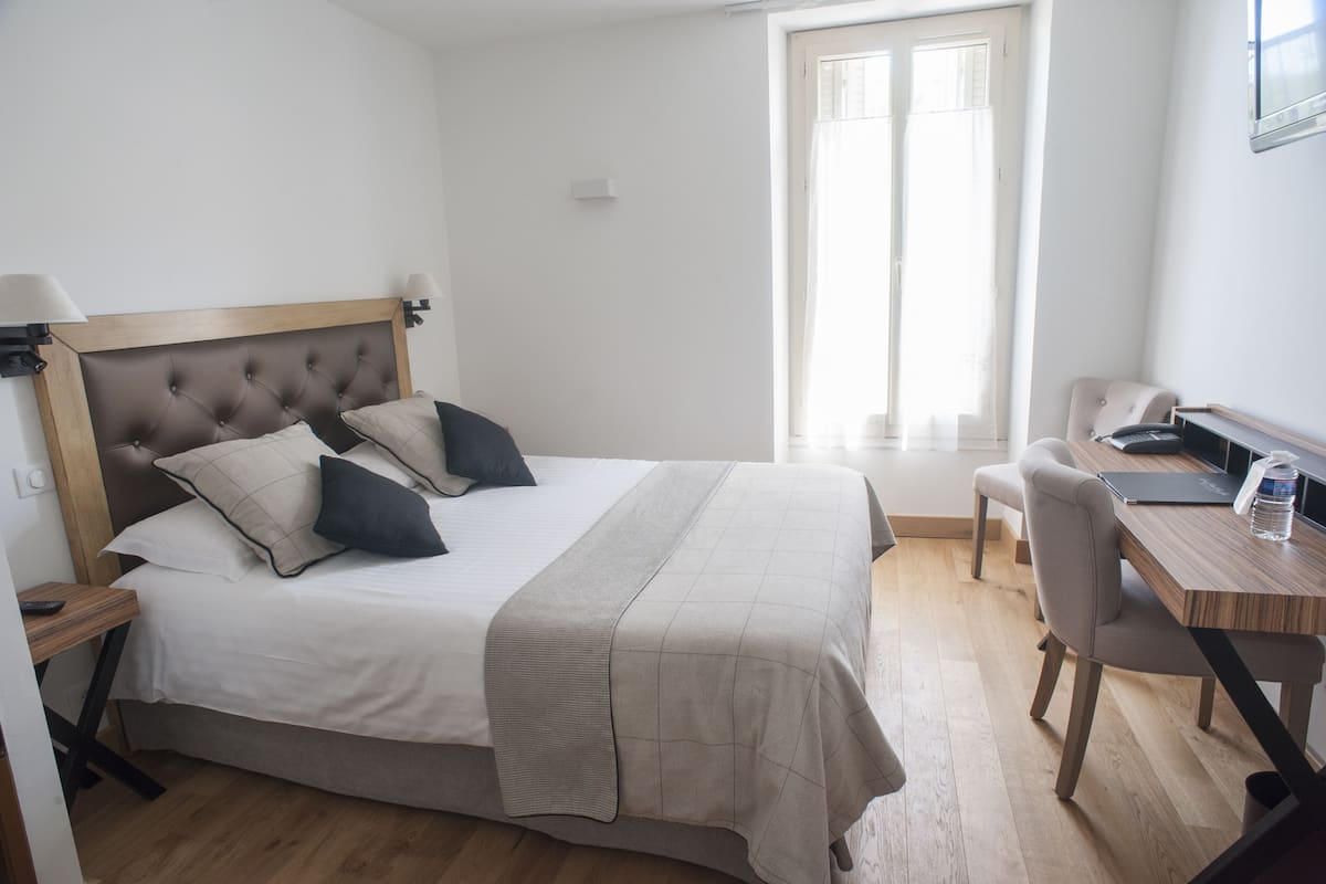 Een verzorgde slaapkamer met een bed, nachtkastje, lamp en een bureau met stoel.