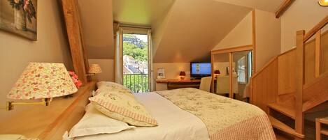 A bedroom with a bed, a desk with a computer, a window with a view, and a staircase.