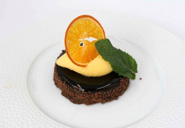 Un postre en un plato blanco con una rodaja de naranja y una hoja de menta encima.
