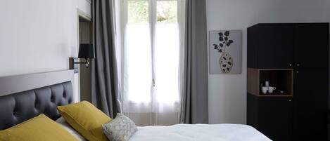 Un dormitorio con una cama, dos almohadas, una mesita de noche, una lámpara, un armario y una ventana con cortinas.