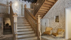 Una escalera de madera con un fondo de pared de piedra, una puerta blanca y dos sillas amarillas.