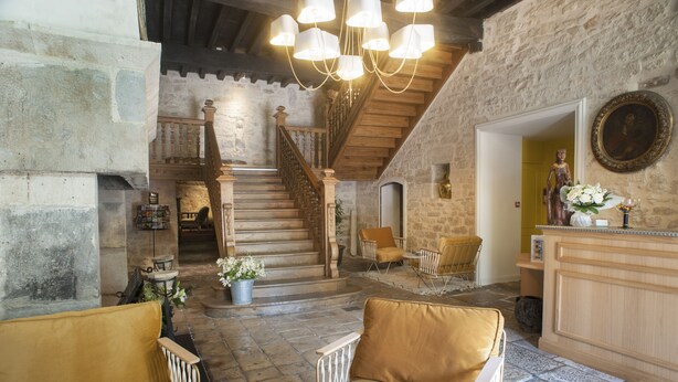 Un interior rústico con una escalera de piedra, muebles de madera y una araña.