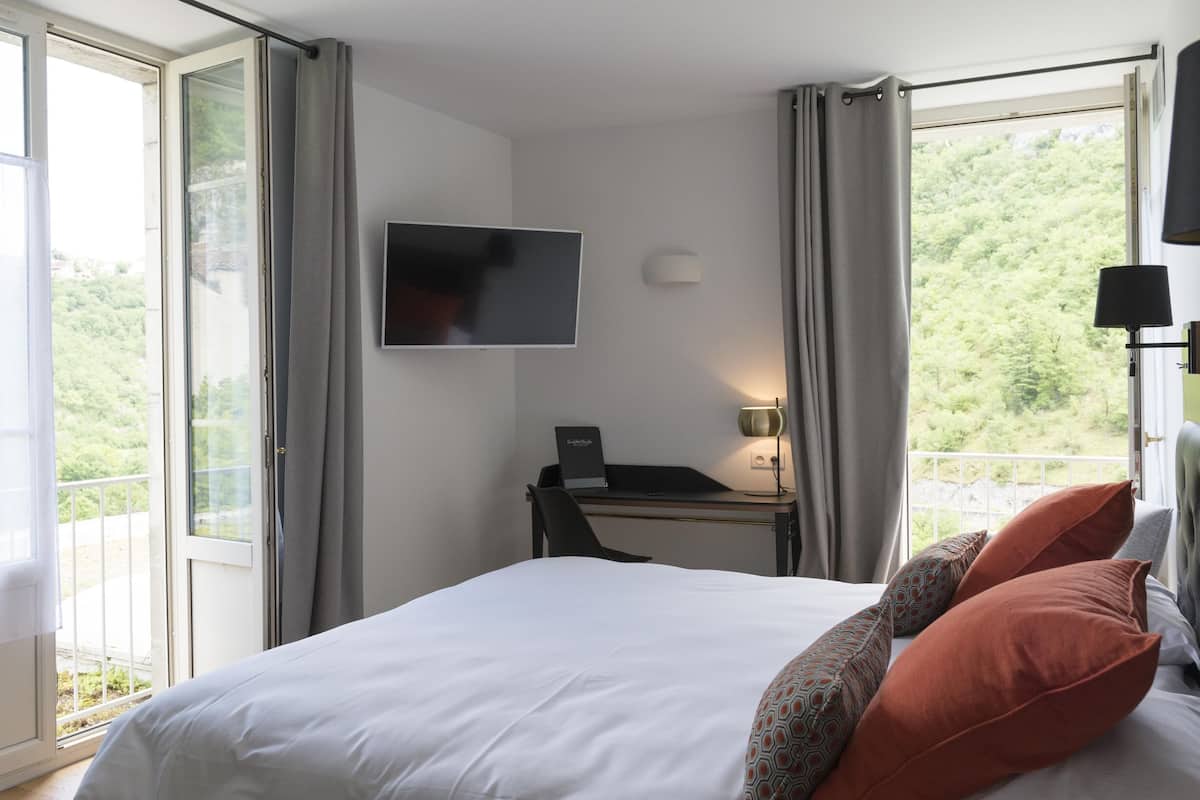 Een hotelkamer met een bed, een bureau met een computer, een televisie en een balkon met gordijnen.