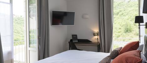 Habitación de hotel con cama, escritorio con computadora, televisor y balcón con cortinas.
