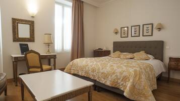 Habitación de hotel con cama, escritorio, silla, lámpara y ventana con cortinas.