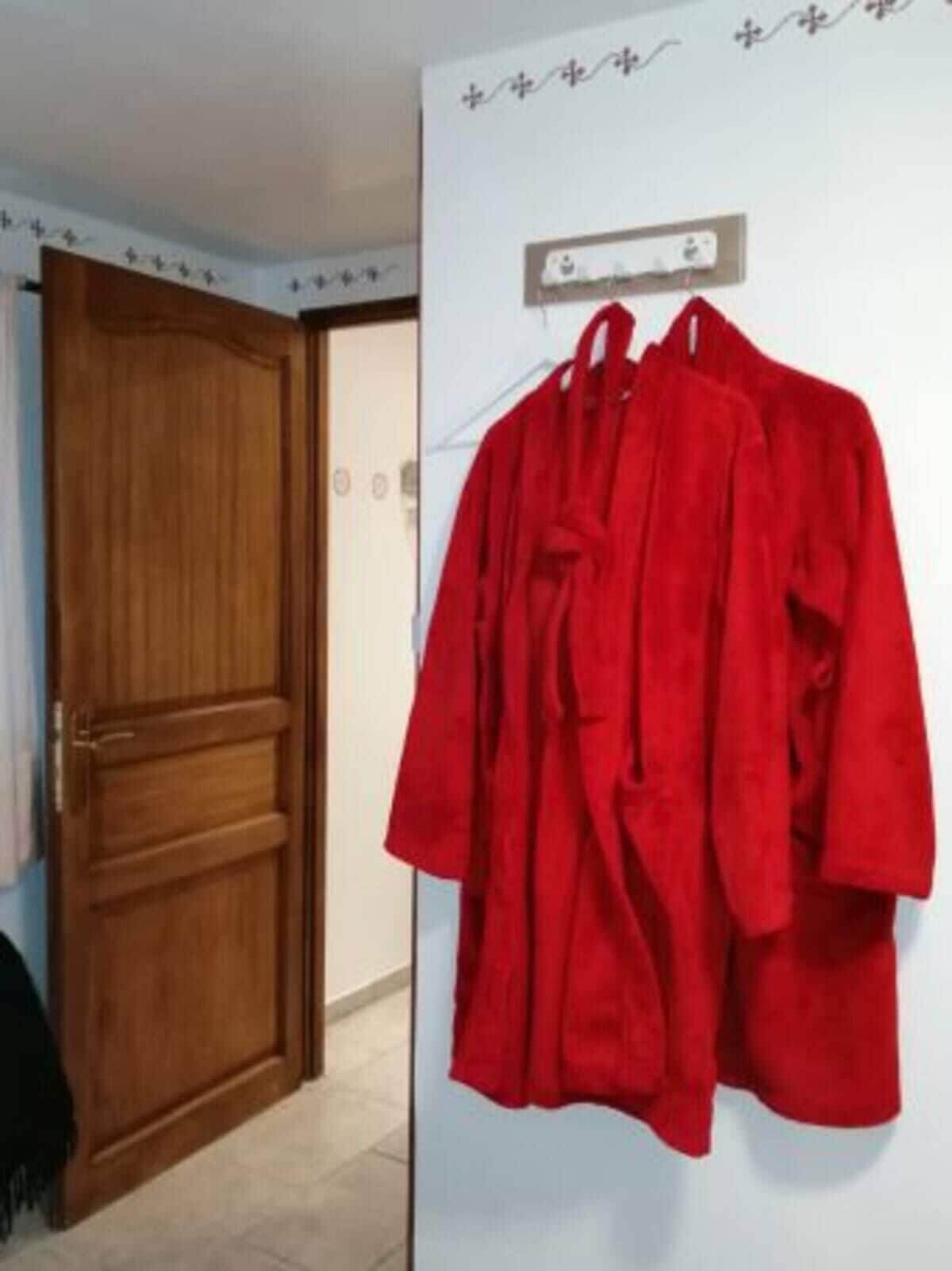 Een kamer met een houten deur, een witte muur met een stopcontact en twee rode gewaden aan de wand.