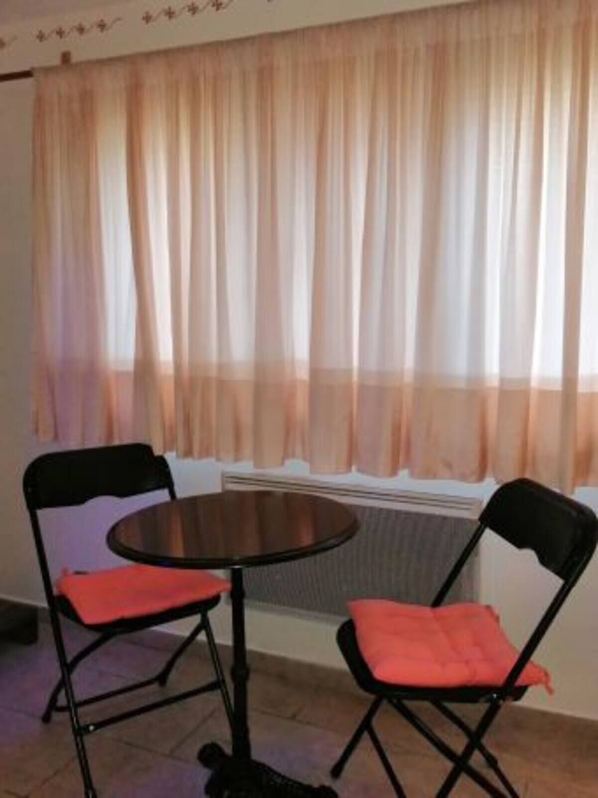 A room with a round table and two chairs, a window with sheer curtains, and a radiator below the window.