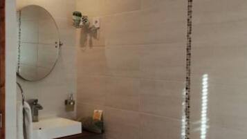 A bathroom with a white sink, a mirror, a towel rack, and a red trash bin.