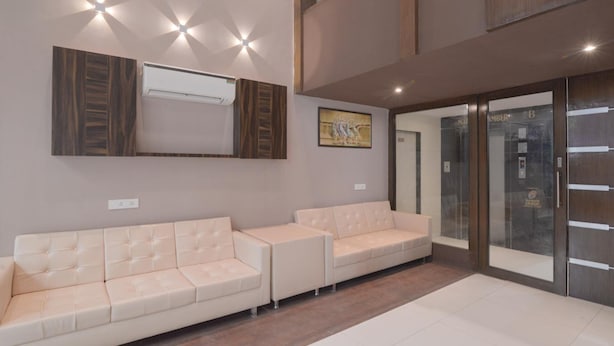 A modern waiting area with two cream-colored sofas, a mounted air conditioner, and a glass door leading to a hallway. - Hotel West Blue (Mumbai)