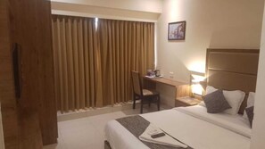 A hotel room with a bed, a desk, a chair, and a window with curtains. - Hotel West Blue (Mumbai)