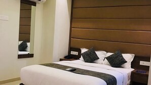 A modern hotel room with a large bed, a ceiling fan, an air conditioning unit, a bedside table, and a nightstand. - Hotel West Blue (Mumbai)