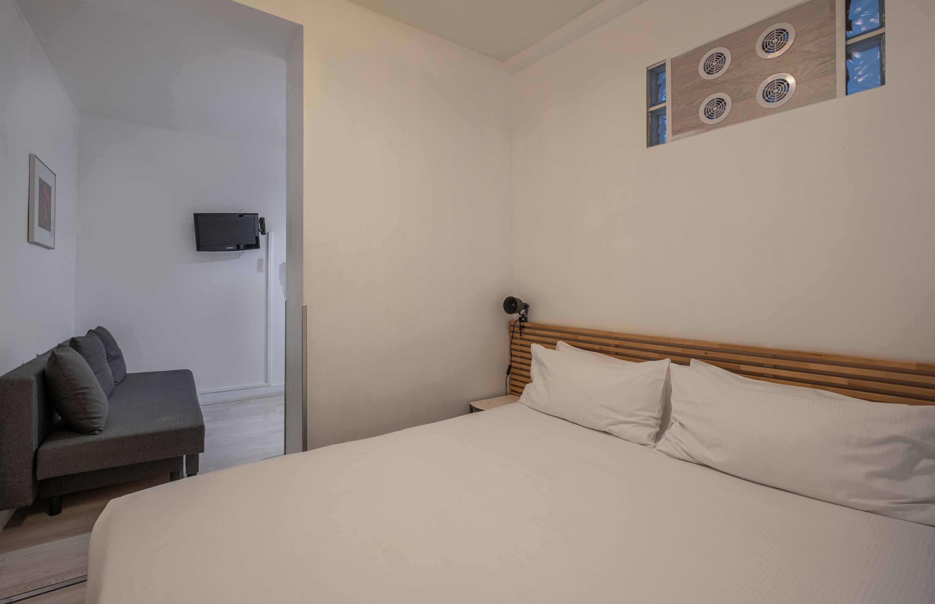 Ein Schlafzimmer mit einem Bett, einem Nachttisch, einem an der Wand befestigten Fernseher und einer Couch.
