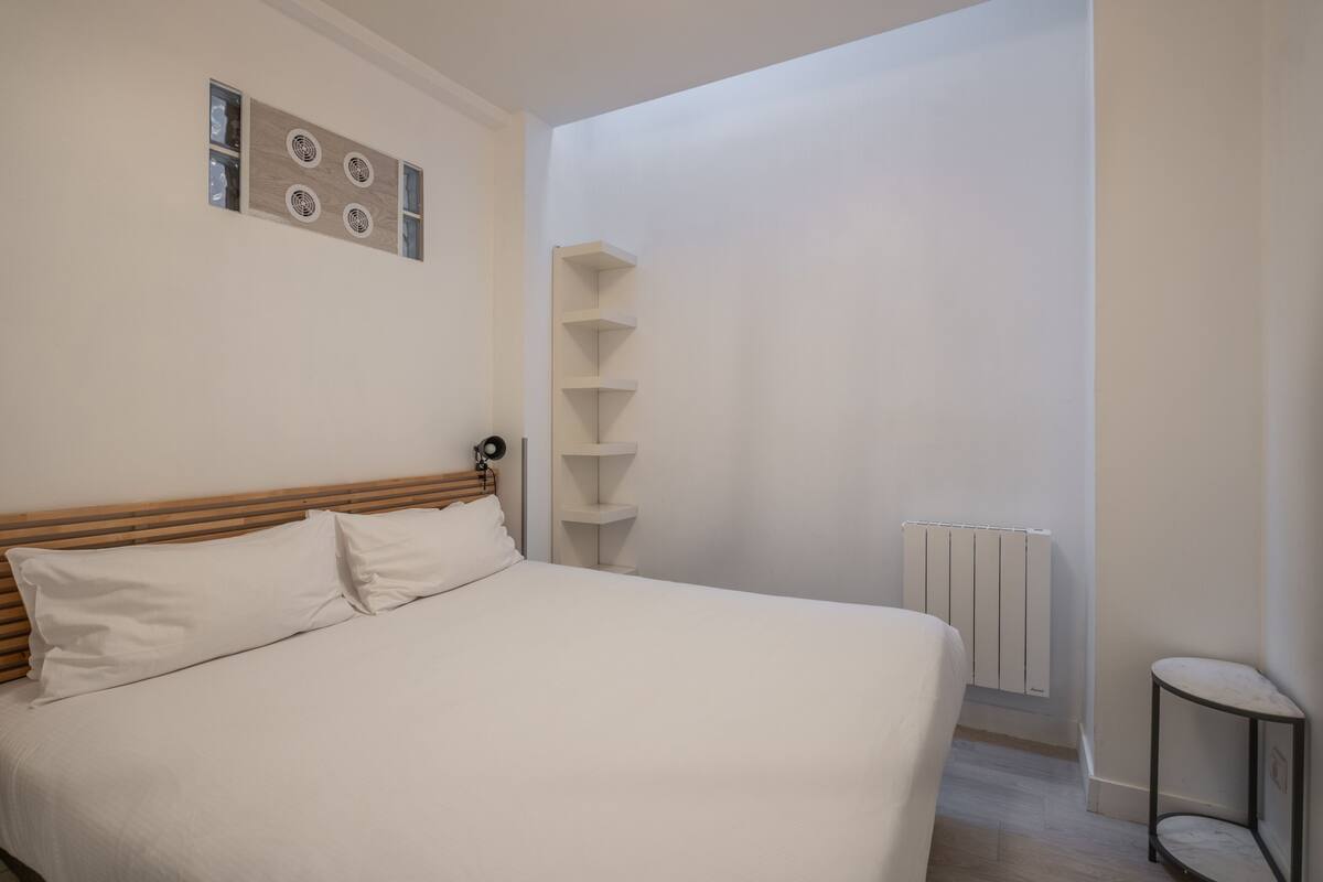 A bedroom with a wooden headboard, a white bed, a radiator, and a small side table.
