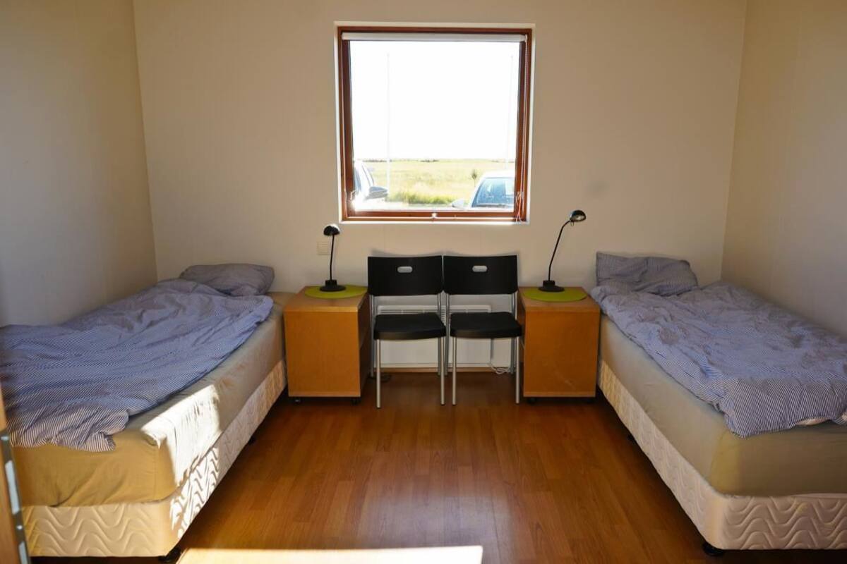 Eine kleine, einfache Unterkunft mit zwei Einzelbetten, einem zentralen Schreibtisch mit Stühlen und einem Fenster mit Blick ins Freie.