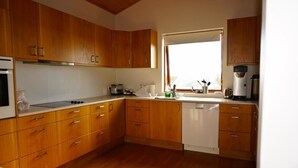 A kitchen with wooden cabinets, a dishwasher, and a window providing natural light. - Guesthouse Uggi (Rangárþing ytra)