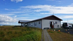 A single-story building with a sloped roof, a porch, and a paved entrance. - Guesthouse Uggi (Rangárþing ytra)