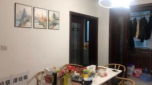 A dining area with a table cluttered with various items, a wall with three framed paintings, and a bright ceiling light. - Pinkhostelling laternational (Shanghai)