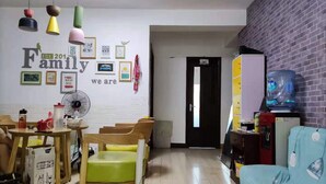 A cozy living area with a white brick wall, a wooden table with chairs, a blue sofa, and a water dispenser. - Pinkhostelling laternational (Shanghai)