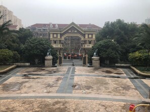 A building with a symmetrical facade, a central entrance, and a surrounding landscaped area with trees and a paved walkway. - Pinkhostelling laternational (Shanghai)