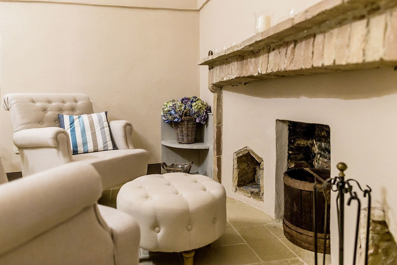 Una sala de estar acogedora con chimenea, un sillón mullido, un otoman a juego y una cesta de mimbre con flores.