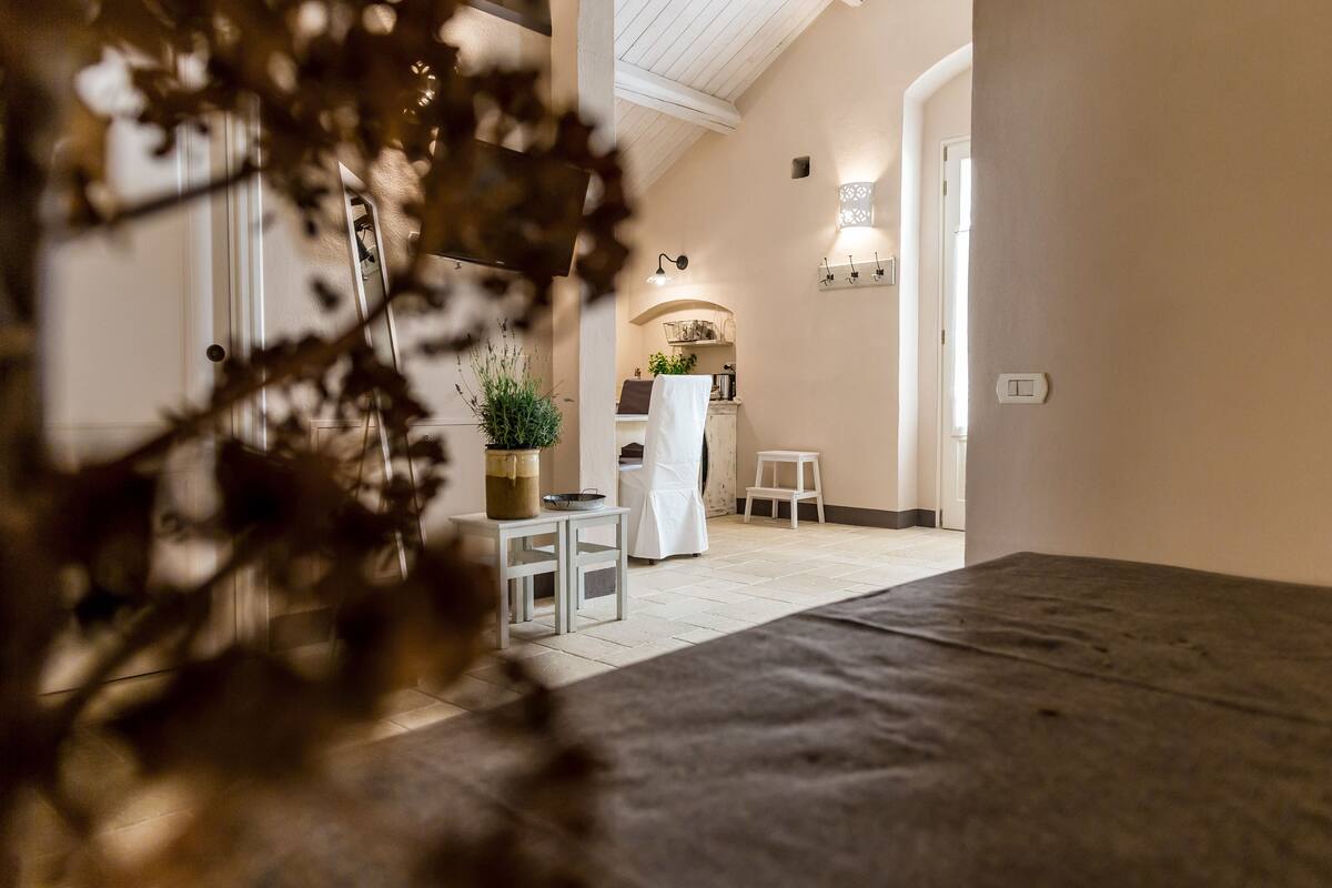 A room with a bed, a small table, a chair, and a potted plant.