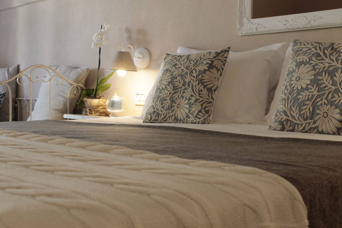 A neatly made bed with floral pillows, a bedside lamp, and a small plant on the nightstand.