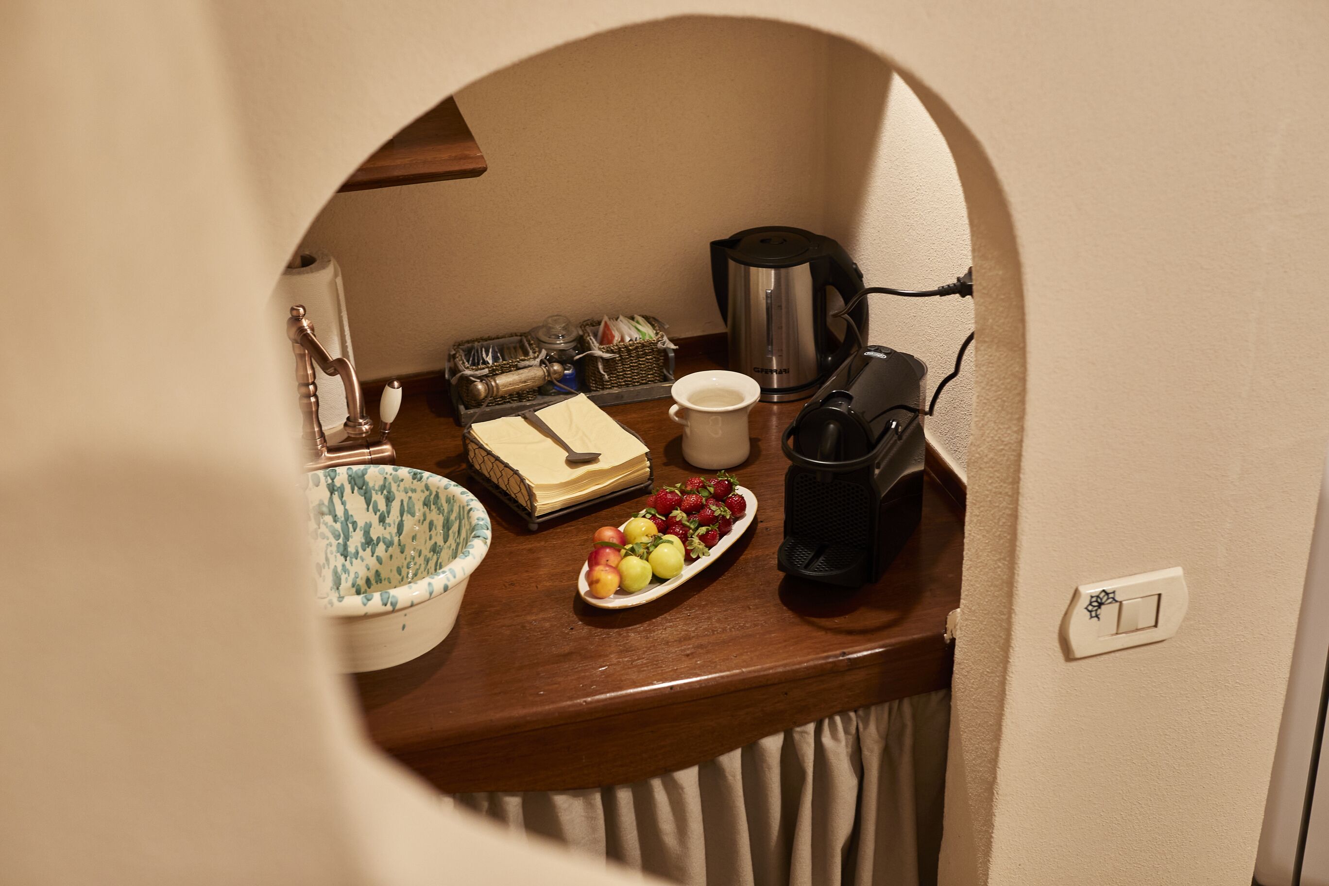 Una kitchenette con cafetera, un cuenco de fruta, un libro y una taza.