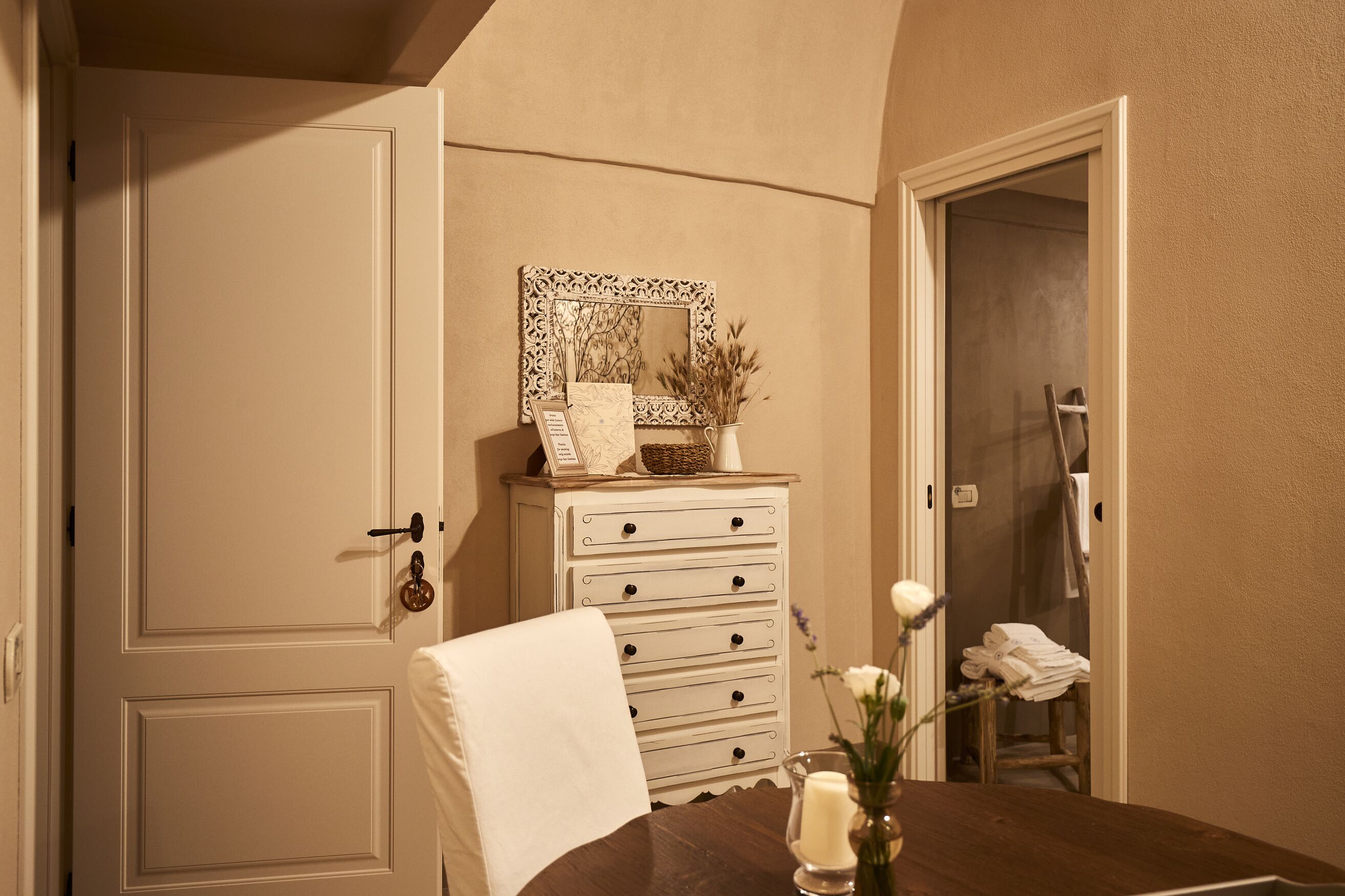 A room with a wooden dresser, a mirror, a vase with flowers, and a chair.