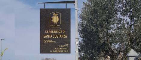A signboard for Le Residenze di Santa Costanza, listing the names of the residences: Le Dimore, Il Mirto, Il Lentisco, Il Corbezzolo.