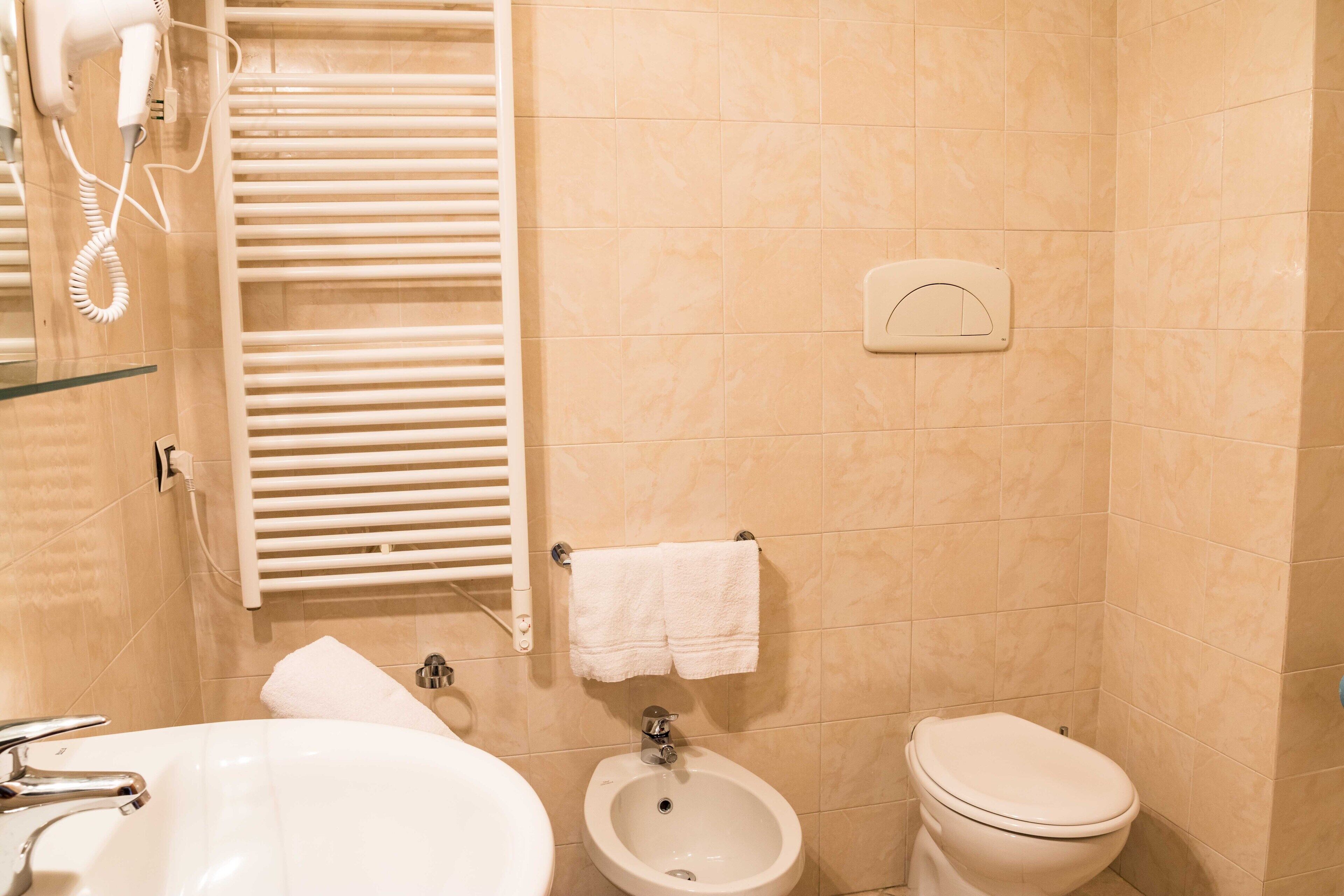 A bathroom with a sink, bidet, toilet, towel rack, and a hairdryer.