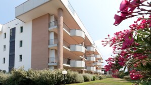 A modern multi-story building with balconies, surrounded by greenery and flowering plants. - Residence Santa Costanza (San Vincenzo)