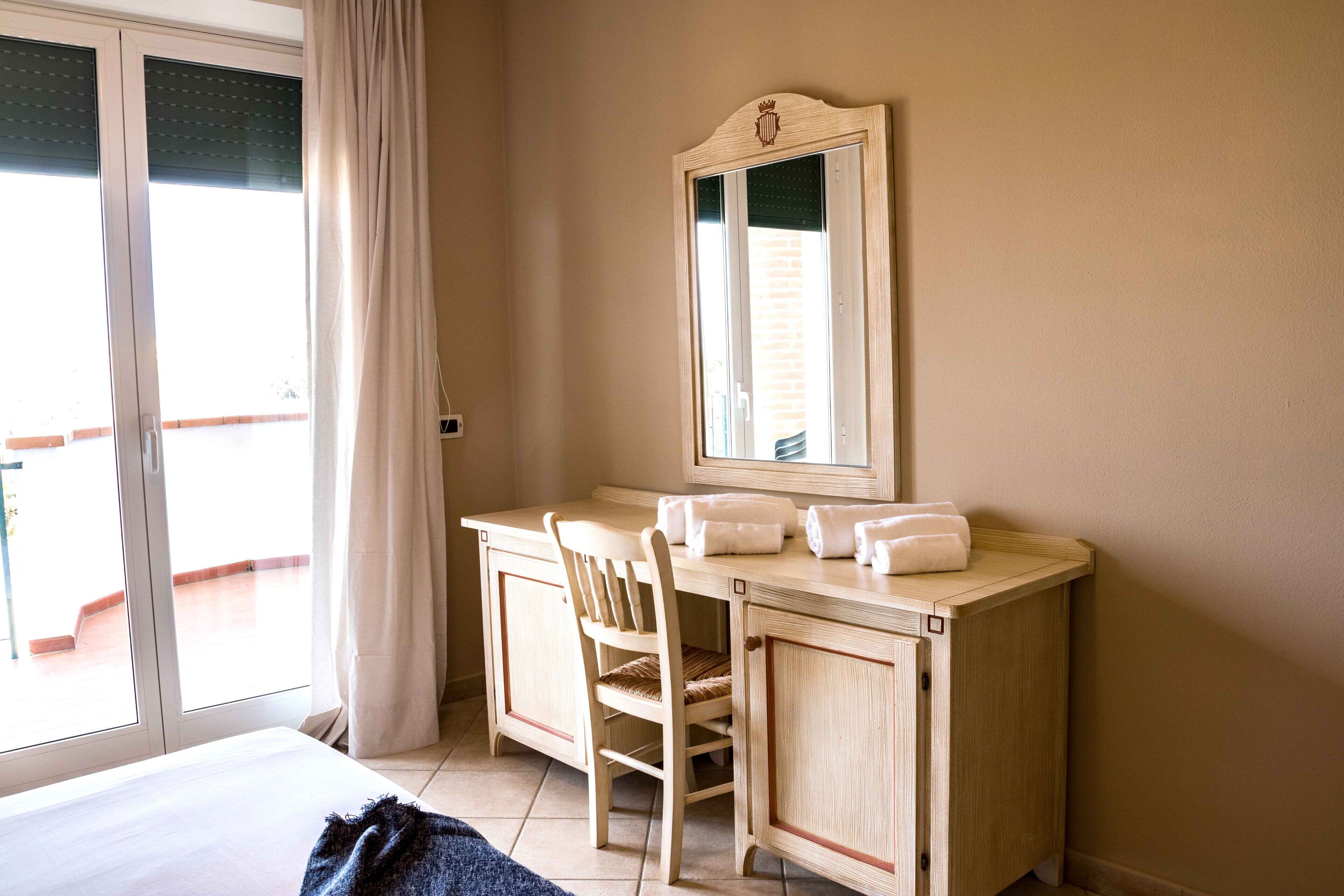 Ein Hotelzimmer mit Bett, Schreibtisch mit Stuhl, Spiegel und einem Fenster mit Vorhängen.