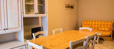 A dining area with a wooden table and white chairs, a sofa with a checkered cushion, and white cabinets with glass doors.