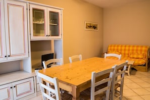 A dining area with a wooden table and white chairs, a sofa with a checkered cushion, and white cabinets with glass doors. - Residence Santa Costanza (San Vincenzo)