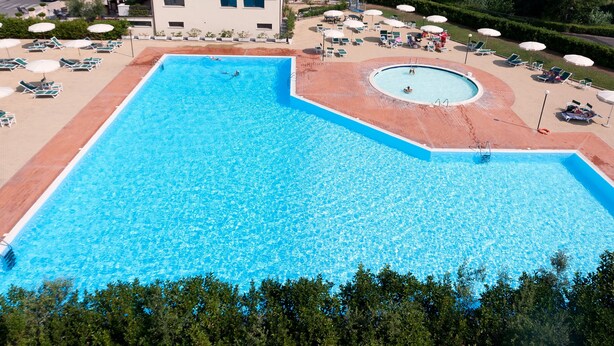A large rectangular swimming pool with a circular section, surrounded by lounge chairs and umbrellas. - Residence Santa Costanza (San Vincenzo)