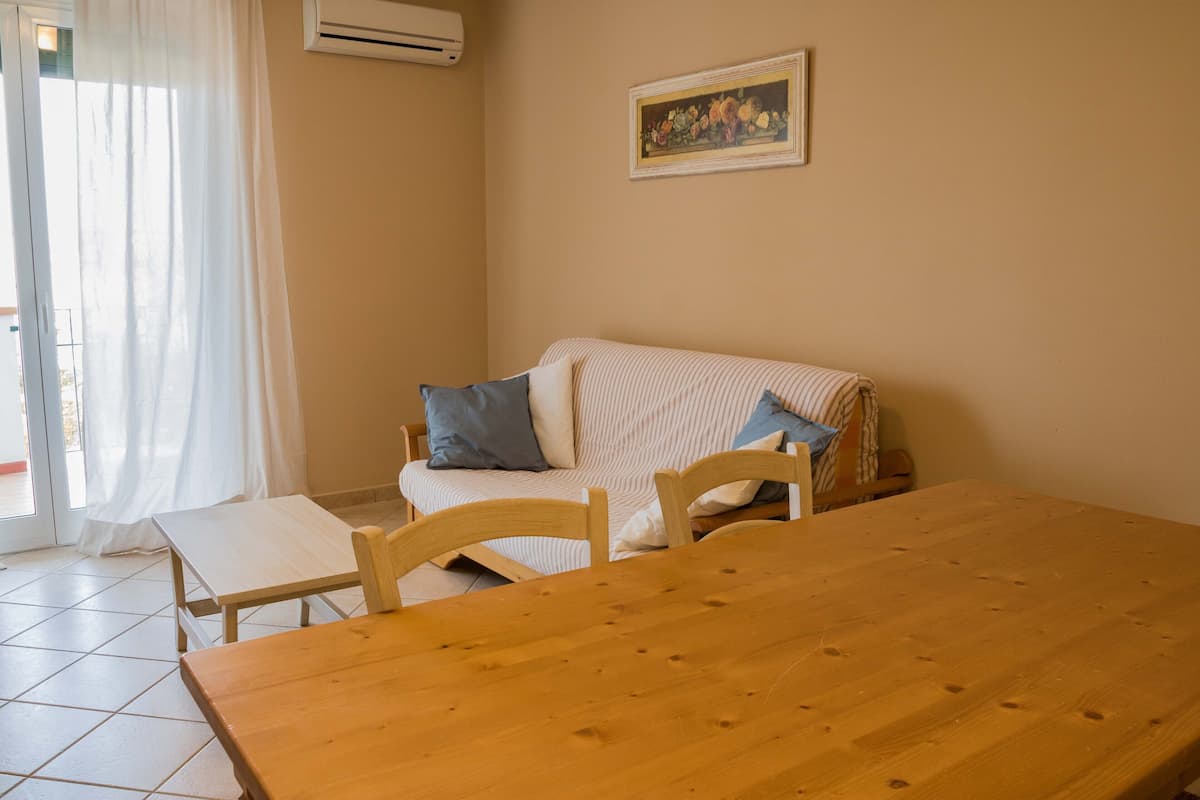 Een kamer met een houten tafel, een gestreepte bank en een schilderij aan de muur.