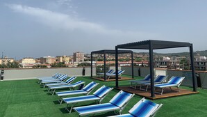 A rooftop terrace with rows of blue-striped lounge chairs and a wooden deck area. - Residence Santa Costanza (San Vincenzo)